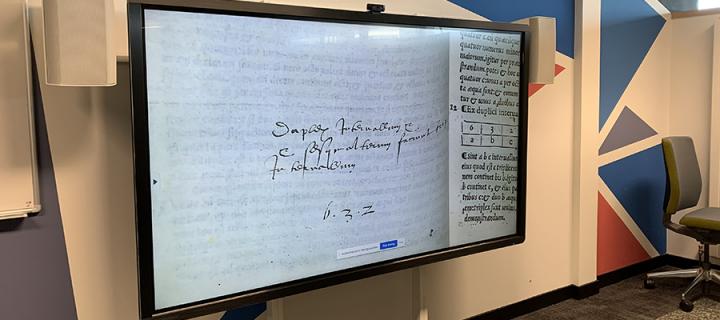 a large screen shows a close-up image of a manuscript