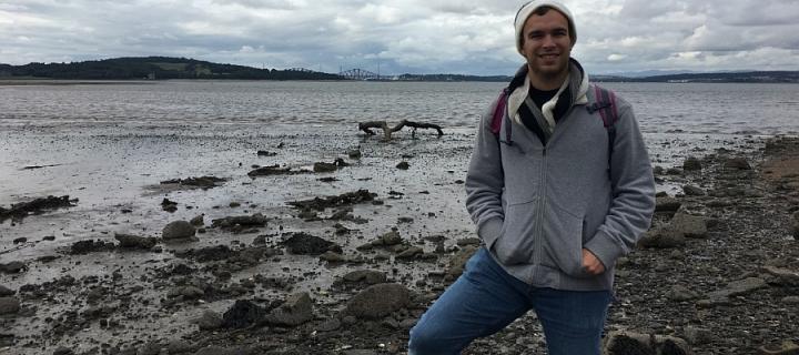 James Theike standing on a rocky beach with Forth Bridges in the distance