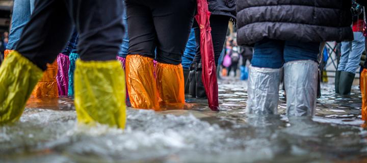 A photo showing several people's legs wearing wellington boots as they wade through floodwaters
