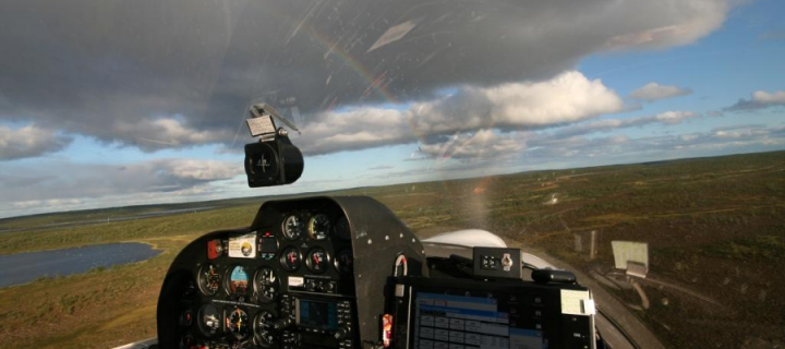 View from an airplane cockpit in the air, showing skies, green landscape and a rainbow 