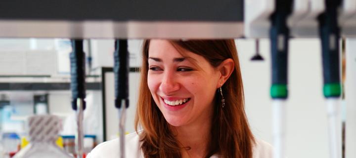 Close up of a white woman in a lab. She is wearing a labcoat and smiling 
