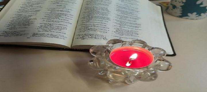 Image of an open book, with a small candle lit beside it. 