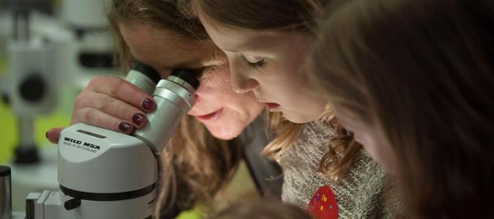 A woman looks through a microscope with two young girls