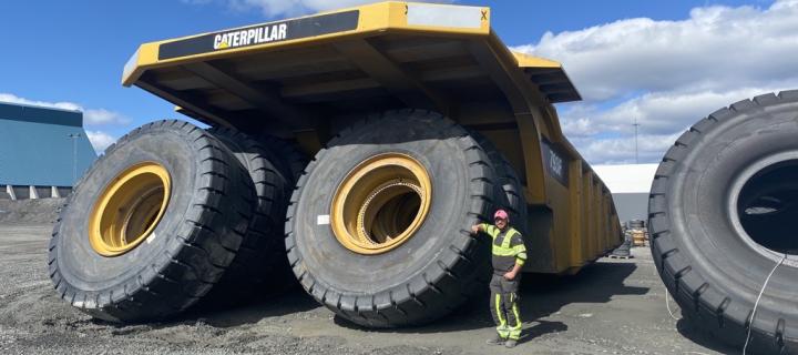 David stands leaning against a Caterpillar vehicle with enormous wheels - they are double his height