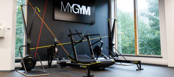 Image with 2 SkiErgs and 2 RowErgs and a Skillmill in front of a black wall with a light box sign saying MyGym