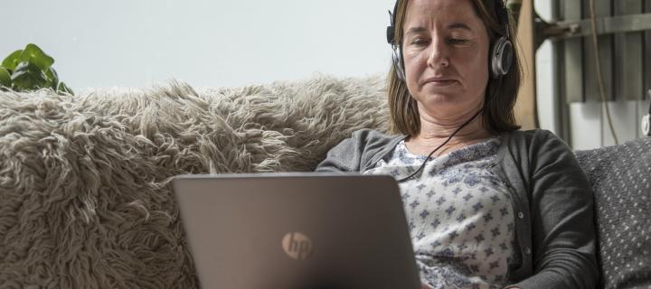 An image of a computer user sitting with a laptop and a headset on the sofa