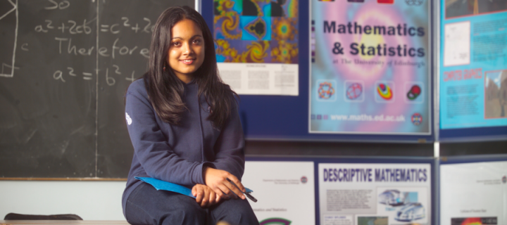 Female student sitting on desk in Maths classroom