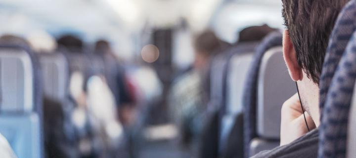 looking down the aisle of a plane or train, over shoulder of person wearing headphones.