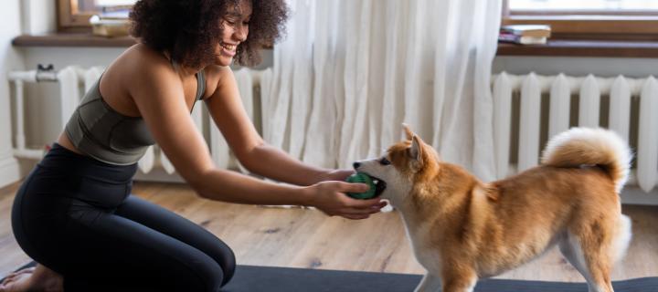 A woman sitting on a yoga mat playing with her dog