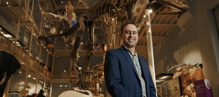 Steve Brusatte stands in front of a dinosaur skeleton smiling to camera