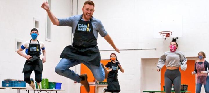 People jumping in scran academy aprons