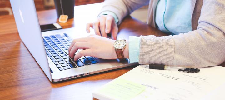 Picture of a student studying at a laptop with notebooks and a coffee