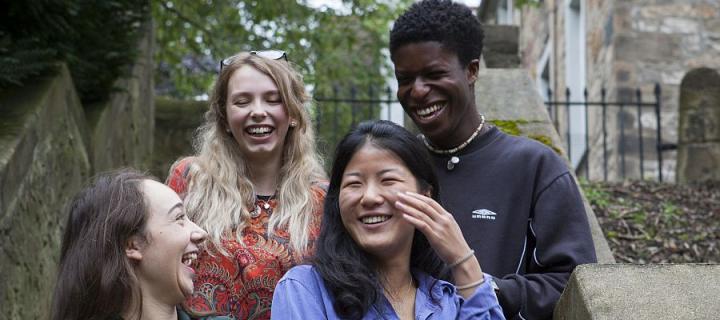 Close up of four Divinit students laughing together outside on the steps in New College garden