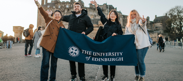 Four students stand in front of Edinburgh Castle with a Edinburgh Uni banner