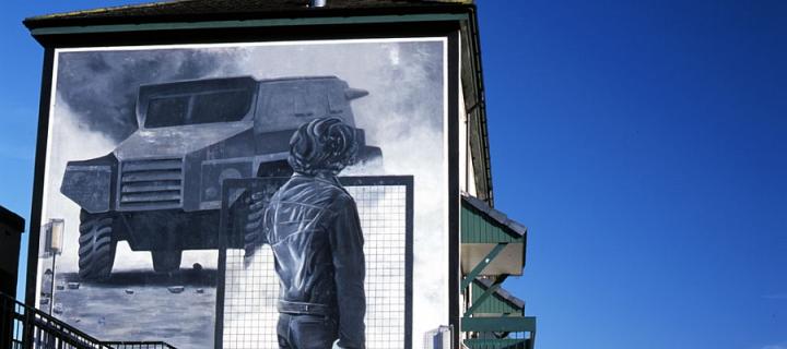 The Rioter mural - a gray painting on a building showing a rioter with a wire mesh shield facing an armoured car