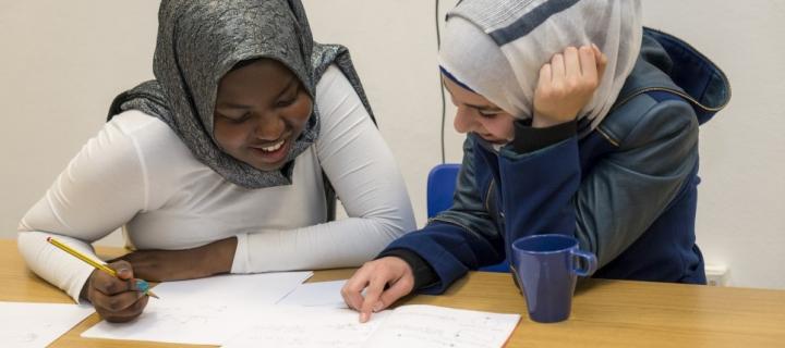 Photograph of Esti Zaid tutoring a student, both are sat at a table looking at books on the table together. 