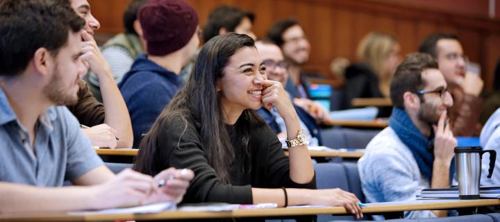 Students sat in lecture theatre smiling and engaging with each other. 