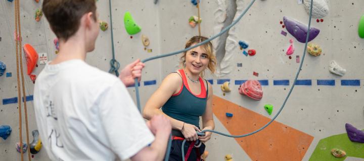 A photo of two people harnessed preparing to climb a climbing wall