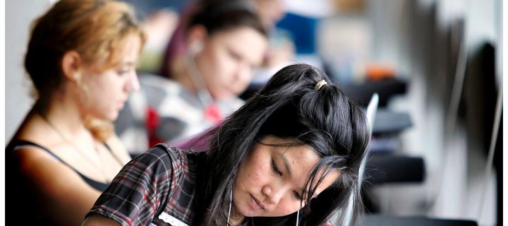 woman with black hair in foreground of row of students studying at desks