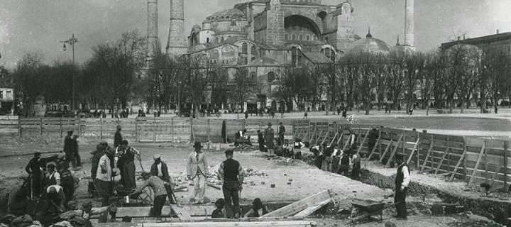 A black and white image showing an archaeological dig in front of a mosque