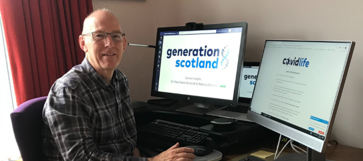 David sat at his computer with one monitor displaying the CovidLife logo and the other displaying the Generation Scotland Logo