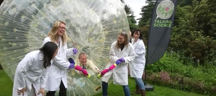 A group of researchers in lab coats stand beside the zorb ball