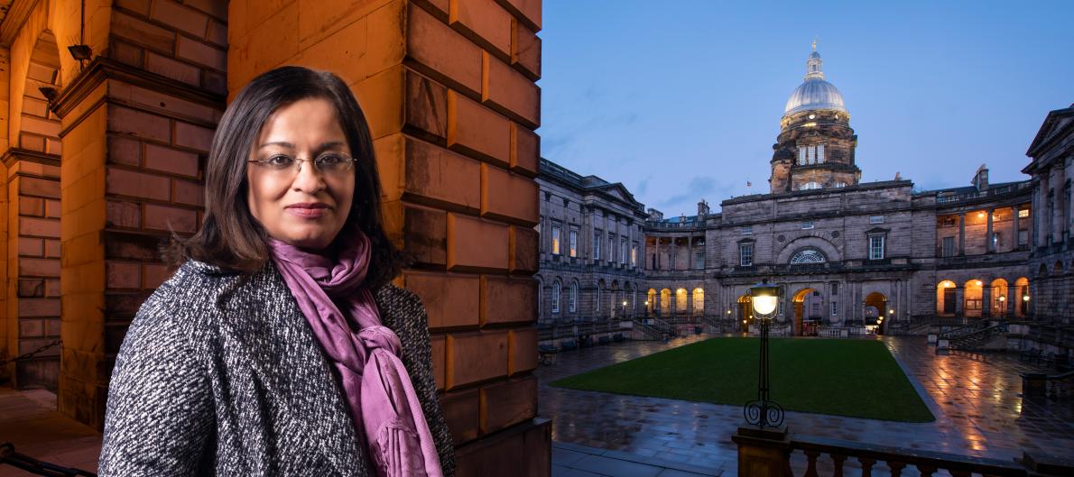 Mona Siddiqui stands in front of Old College building at dusk.
