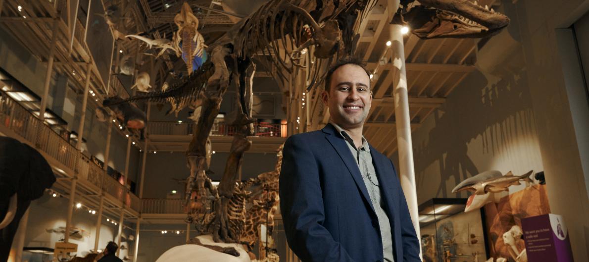 Steve Brusatte stands underneath a dinosaur skeleton smiling to camera.