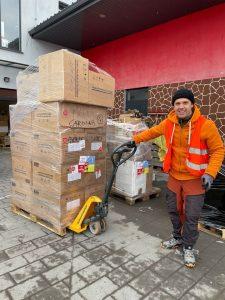 Volunteer standing next to a tall stack of donations contained in cardboard boxes