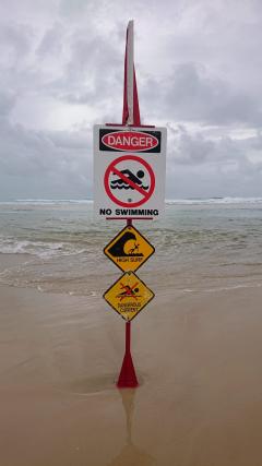 A no swimming sign on the beach with a stormy sky.
