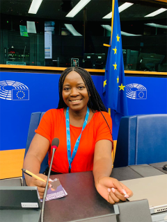 Amanda Wanyonyi is sat at a desk at the European Student Assembly with the flag of Europe behind her
