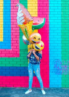 person holding big balloons in front of a colourful wall