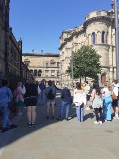 A group of people are being led on a tour of the University of Edinburgh, with McEwan Hall on the right.
