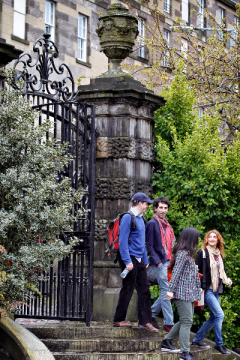 A group of university students walking through a gate and down stone steps outside a building in Edinburgh
