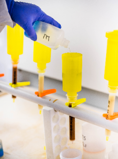 A close view of blue gloved hands dropping chemicals into yellow scientific receptacles for anion analysis