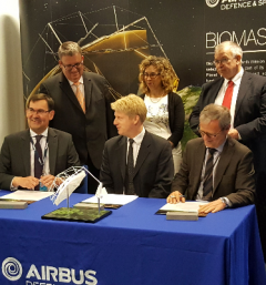 European Space Agency BIOMASS satellite contract signing, with 6 staff behind a table displaying a contract and satellite model