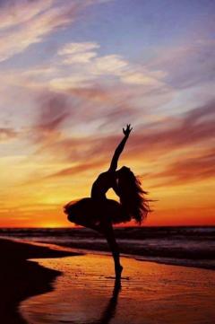Silhouette of a ballet dancer on a beach at sunset. The sunset is a mixture of red, yellow and orange colours and the sunset is reflecting on the wet sand where the dancer is standing. 