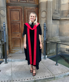 Dr Emma Kinley in a black and red graduation gown outside McEwan Hall, University of Edinburgh