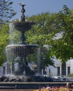 Picture of a two tiered fountain outside in the sunshine. Water is overflowing from each of the tiers into the bottom. 