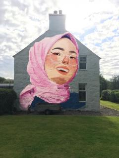 Image of a girl wearing a hijab painting onto the gable end of a house