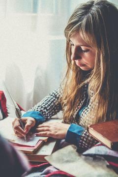 Photograph of a teenage girl writing in a book at a desk. 