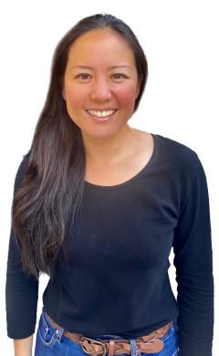 Photograph of Lilian Lee, Chaplaincy Listener. Lilian is standing in front of a white background, wearing a black t-shirt and blue jeans