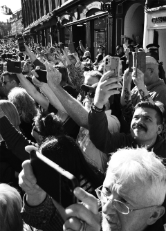 Black and white scene of a crowd of people with their camera phones capturing something out of shot.