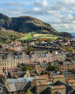 Arthurs Seat sits behind the buildings of Edinburgh on a sunny day.