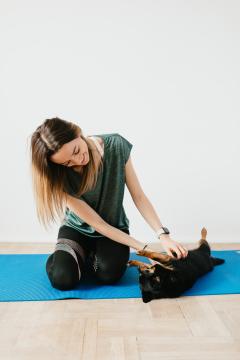 A woman sitting on a yoga mat giving a dog belly rubs