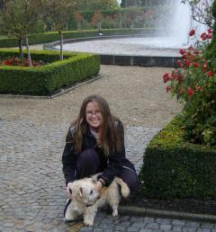 Photograph of Associate Chaplain Urzula Glienecke crouched down patting a dog. Urzula is in a garden with a fountain behind her.