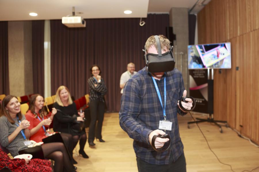 Man playing virtual reality game in Bayes Centre with crowd watching