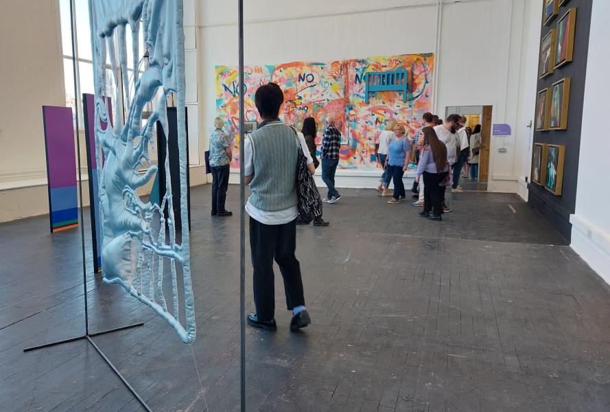 Blue fabric hanging over a metal frame in the foreground. In the background a group of people is looking at another display.