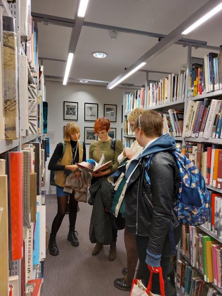 A group of people looking at a book in the ECA library. They are surrounded by shelves filled with colourful books.