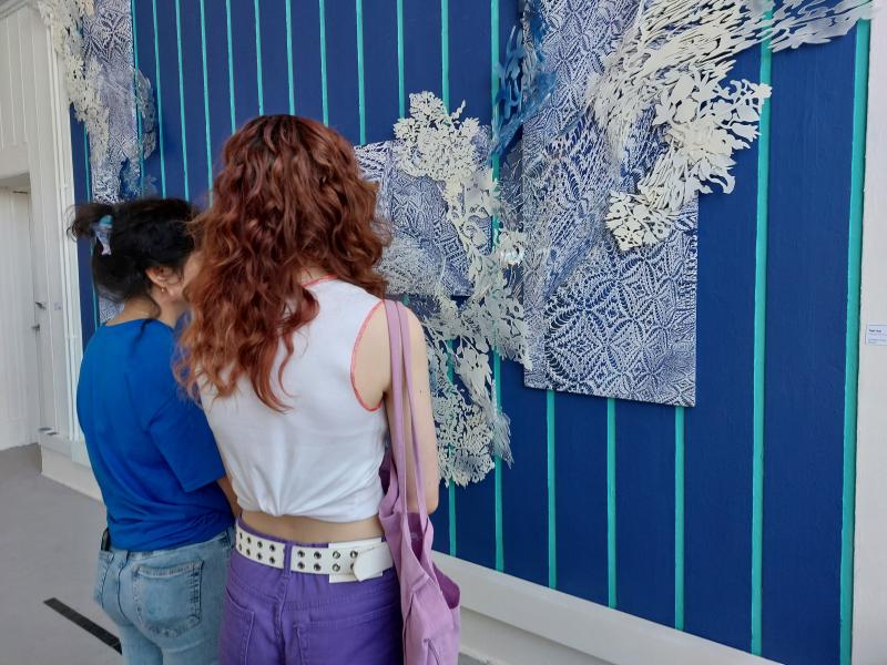 Two people are looking at an art work that fills an entire wall and is coloured in a bright blue.